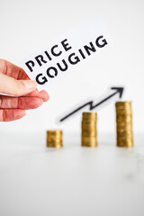 hand holding Price Gouging text in front of growing stacks of coins, symbol of excessive pricing or speculation