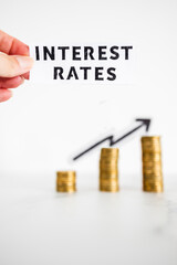 hand holding Interest Rates text in front of growing stacks of coins with arrow going up