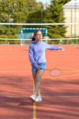 Obraz premium Children and sports. A teenage girl is actively playing badminton. Active lifestyle. Outdoor sport leisure activity. A girl beats a shuttlecock with a racket.