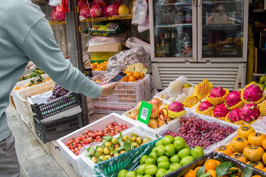 A customer uses his smart phone to pay his purchase at a fruit market stand with Qr code payment. (with altered qr plate)