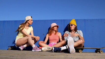 Three friends enjoy a sunny day at the skate park, chatting and relaxing beside their skateboards, showcasing youthful energy and friendship - Powered by Adobe