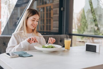 Young woman enjoying healthy salad and orange juice in restaurant