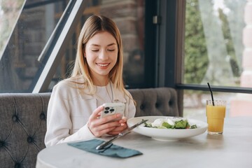 Young woman using smartphone while having lunch in a restaurant