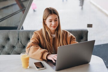 Young woman working on laptop in cafe, drinking orange juice