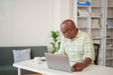 Focused mature African American entrepreneur working on a laptop, managing business tasks, and...
