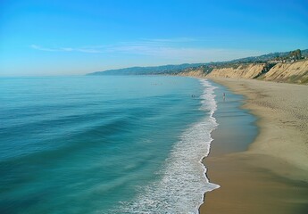 A pristine sandy beach stretches along a calm turquoise ocean, with a line of cliffs in the distance under a clear blue sky