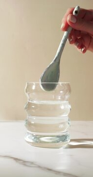 Close-up of a spoon dropping light-colored powder&mdash;ideal for creatine, electrolytes, or collagen&mdash;into a clear glass of water, followed by gentle stirring. Clean, soft lighting, health, hydration