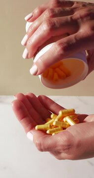 Close-up of yellow capsules pouring from a white supplement bottle into an open palm. Bright natural light and a clean backdrop convey daily wellness routines, nutrition, and health-focused lifestyles