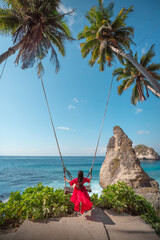 Girl sitting on a swing at Diamond Beach in Nusa Penida Island, Bali, Indonesia. A beautiful and popular beach with large rocks resembling large diamonds standing tall in the middle of the blue sea.