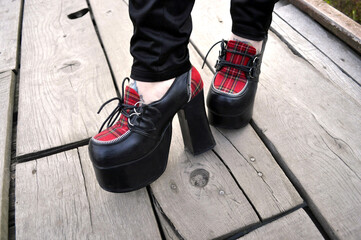 legs of a girl in gothic black shoes with high soles and high heels. red check on shoes. informal...