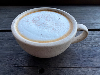 Hot cappuccino coffee in white cup on wooden table background. Art of milk foam circle shape with copy space on brown melt coffee top view
