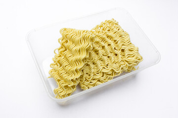 Dried square raw instant noodles inside a plastic container, isolated on white.
