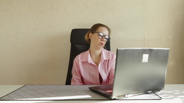 Upset woman in office using laptop, seated indoors at her desk, expressing pity over lost productivity, dealing with stress.