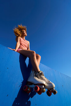 Young woman wearing roller skates sitting on a wall looking away