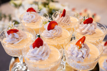 Close-up of multiple glass dessert cups filled with creamy mousse, topped with swirls of whipped cream, strawberry slices, and delicate white flowers