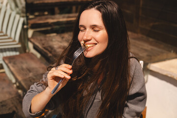 Joyful young woman sitting in cafe with plate of caesar salad, ready to eat a bite of chicken and...