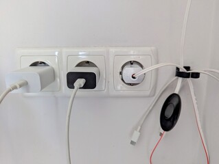 Three white electrical outlets mounted on a wall, each equipped with charging adapters and cable...