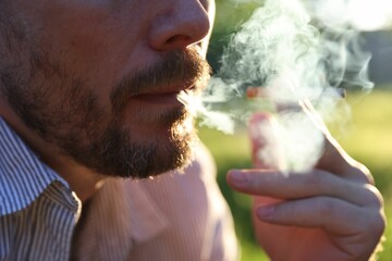 Man smoking cigarette on blurred background, closeup
