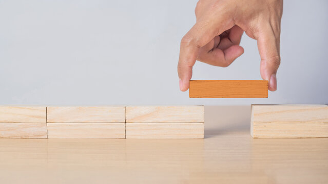 Business concept image showing a man connecting two sides using a orange wooden block, representing finding solutions, bridging gaps, and resolving issues.  growth and support themes