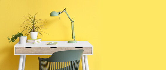 Table with houseplants and desk lamp near yellow wall