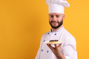 Happy confectioner in uniform holding tart with blueberries on orange background