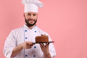 Happy confectioner in uniform holding chocolate cake on pink background