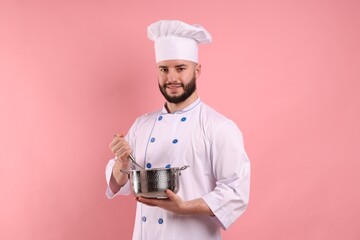 Happy confectioner in uniform holding whisk and cooking pot on pink background