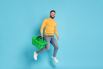 Man with empty shopping basket jumping on light blue background