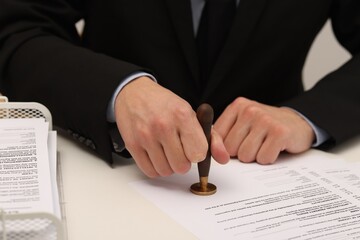 Man stamping licensing agreement document at white table indoors, closeup