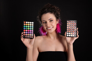 Smiling woman with eyeshadow palettes on black background
