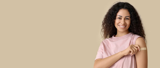 Young African-American woman with medical patch after vaccination on beige background