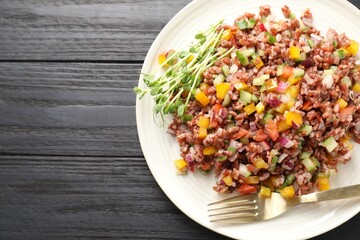 Tasty salad with brown rice on black wooden table, top view. Space for text