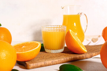 Wooden board with glass and jug of fresh orange juice on white background