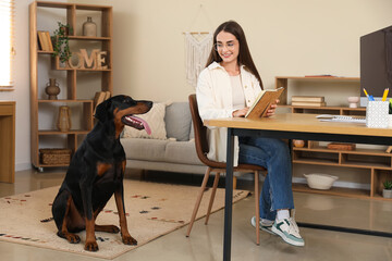 Cute Doberman dog and beautiful young happy woman with book on workplace at home
