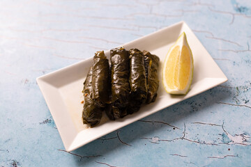 Stuffed grape leaves with lemon wedge on white rectangular plate.
