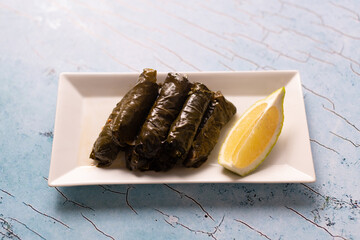 Stuffed grape leaves with lemon wedge on white rectangular plate.
