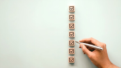 Checklist planning concept with hand holding pen and wooden blocks on blue background