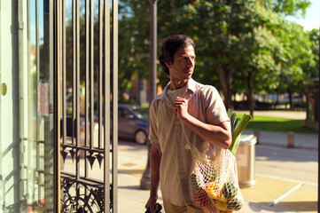 Indian businessman is walking out of a store, holding a reusable shopping bag filled with fresh...
