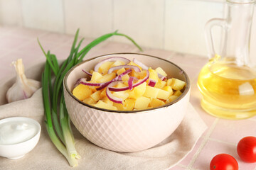 Bowl of tasty potato salad with onion and ingredients on pink tile table