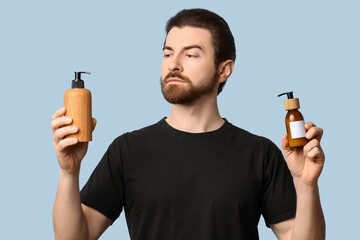 Bearded young man holding bottles of cosmetics on blue background