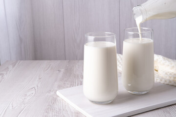 Pouring homemade kefir, buttermilk or yogurt with probiotics. Yogurt flowing from glass bottle on...