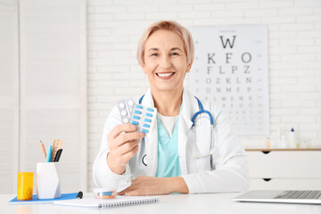 Fototapeta premium Happy mature female doctor with pills sitting in clinic
