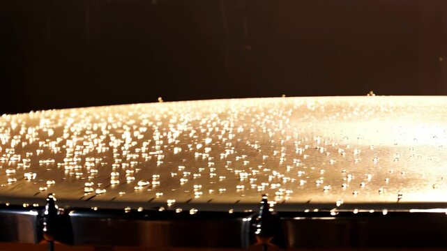 Closeup of water droplets vibrating on timpani drum, illuminated by bright light and music