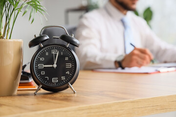 Alarm clock on table against businessman working in office, closeup