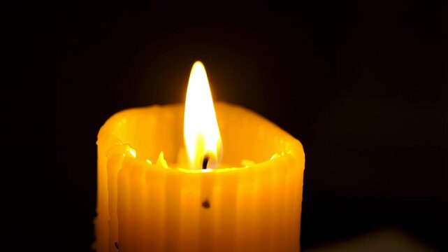 Burning yellow paraffin candle emitting warm light against dark background used for religious rituals or romantic mood setting