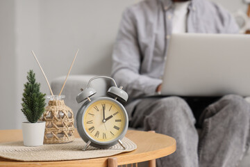 Vintage alarm clock on table against man working with laptop at home, closeup