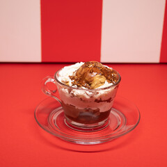 Layered chocolate dessert served in glass cup over red stripes.