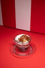 Layered chocolate dessert served in glass cup over red stripes.