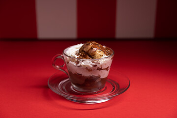 Layered chocolate dessert served in glass cup over red stripes.