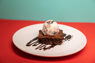 Brownie topped with ice cream scoop and chocolate drizzle, plated.